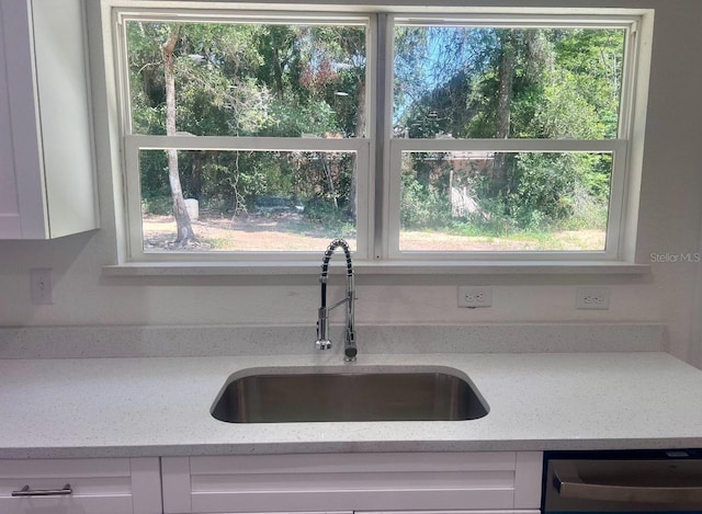 kitchen with light stone counters, dishwasher, white cabinets, and a sink