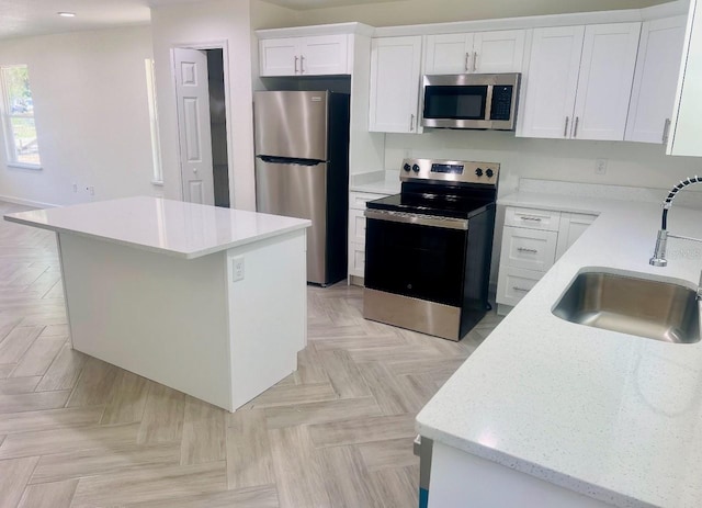 kitchen with light stone counters, appliances with stainless steel finishes, a kitchen island, a sink, and white cabinetry