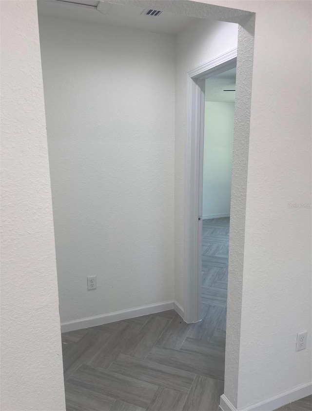 hallway featuring visible vents, a textured wall, and baseboards