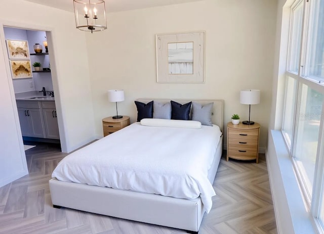 bedroom featuring an inviting chandelier, ensuite bathroom, and a sink