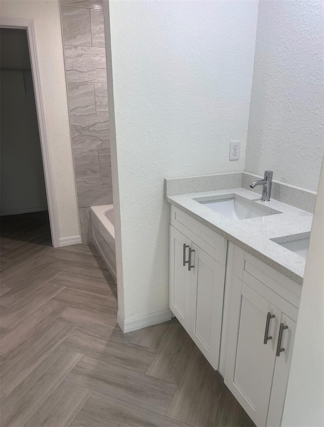 full bathroom with double vanity, a sink, a textured wall, and a tub