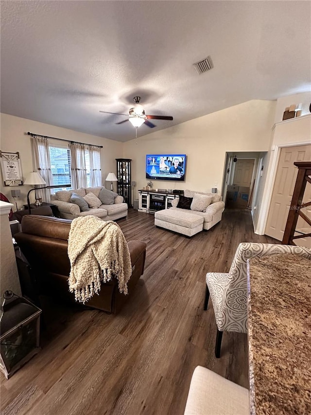 living room with ceiling fan, vaulted ceiling, dark wood-type flooring, and a textured ceiling