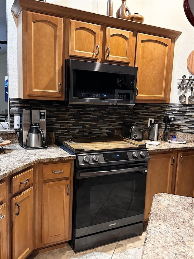 kitchen featuring backsplash, range, light tile patterned floors, and light stone countertops