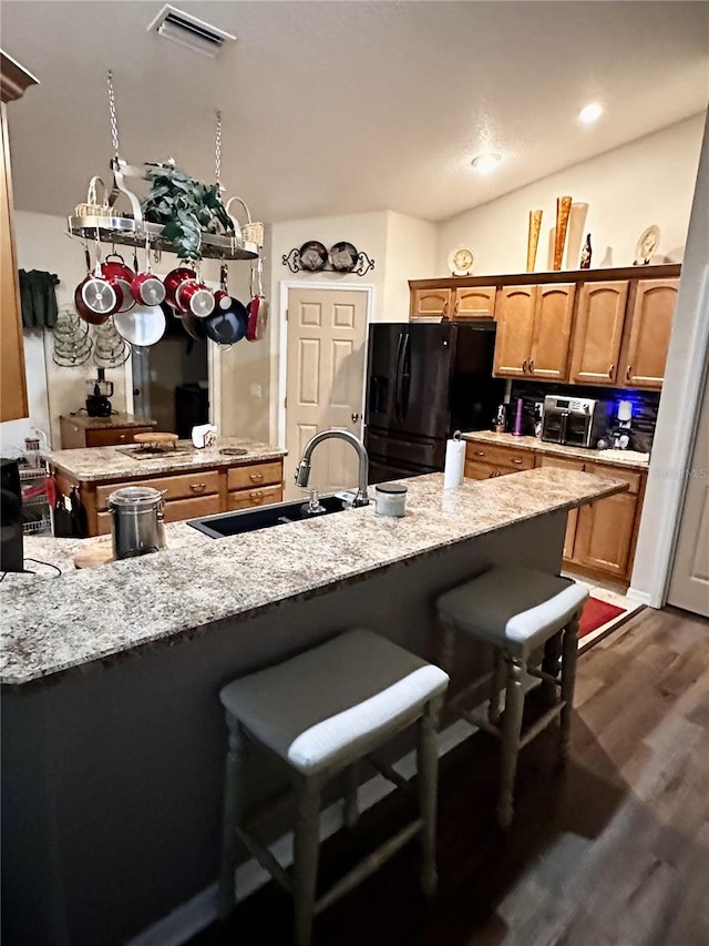 kitchen featuring a kitchen bar, sink, black fridge, dark wood-type flooring, and light stone counters