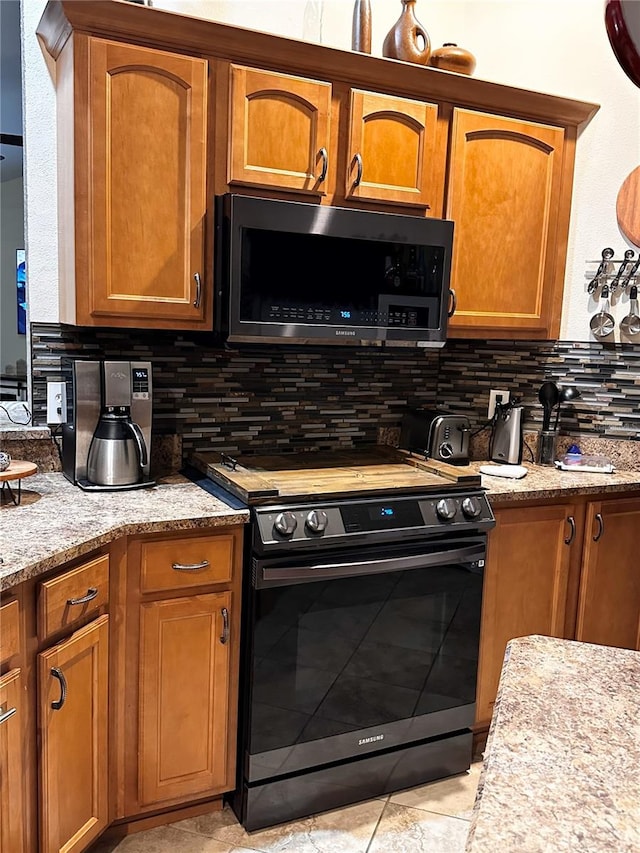 kitchen with light stone countertops, backsplash, light tile patterned floors, and black range oven