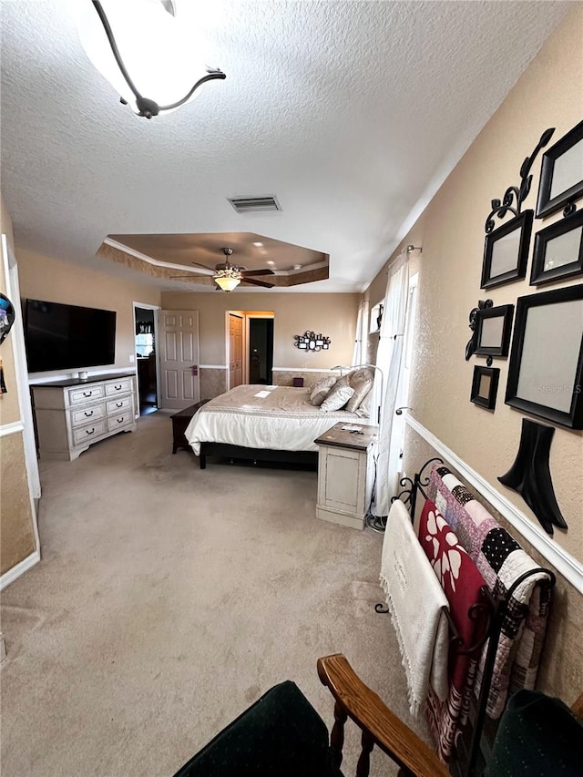 bedroom featuring ceiling fan, a raised ceiling, a textured ceiling, and light carpet