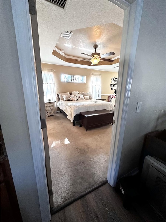 bedroom with hardwood / wood-style flooring, a textured ceiling, a tray ceiling, and ceiling fan