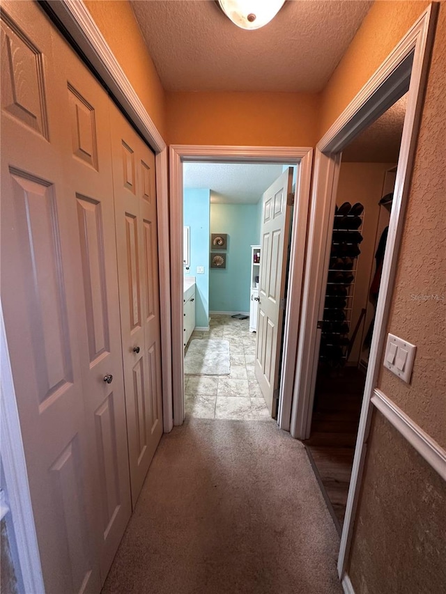 hallway with light carpet and a textured ceiling