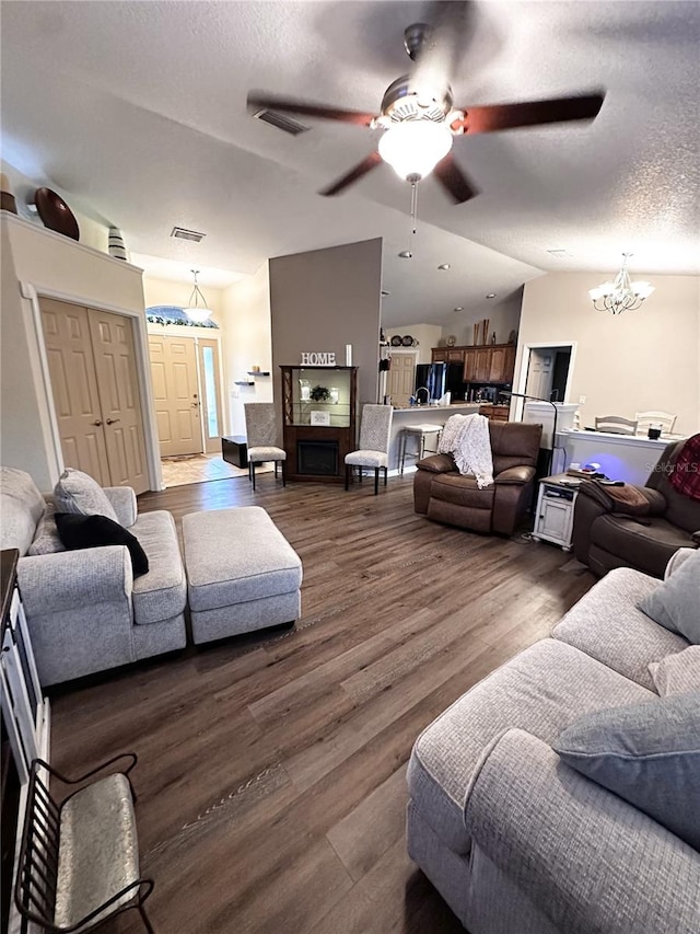 living room with ceiling fan with notable chandelier, a textured ceiling, dark hardwood / wood-style floors, and lofted ceiling