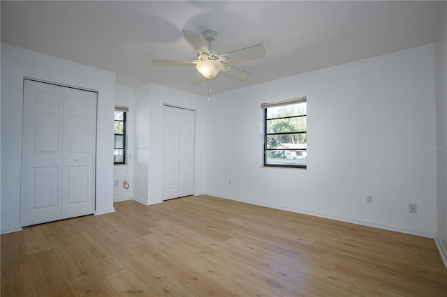 unfurnished bedroom featuring ceiling fan, multiple closets, and light hardwood / wood-style flooring