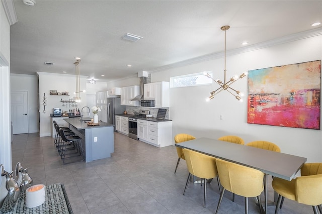 kitchen featuring a kitchen bar, stainless steel appliances, pendant lighting, white cabinets, and an island with sink