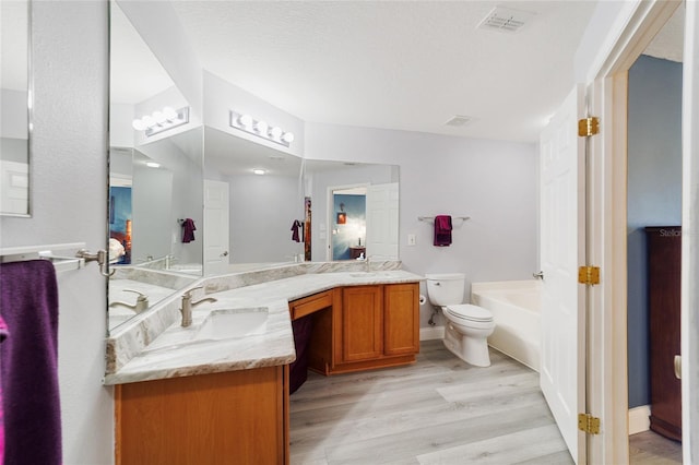 bathroom featuring hardwood / wood-style floors, toilet, a tub to relax in, and vanity