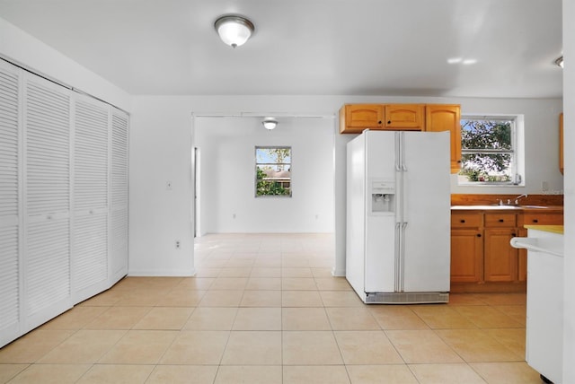 kitchen with light tile patterned flooring, plenty of natural light, white fridge with ice dispenser, and sink