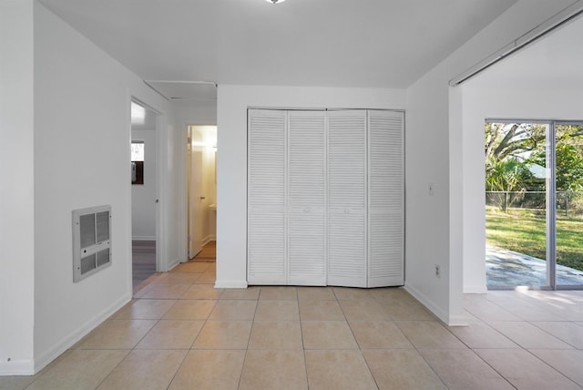 unfurnished bedroom featuring access to exterior, heating unit, a closet, and light tile patterned flooring