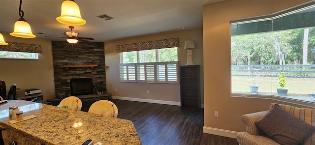 living room with ceiling fan, a healthy amount of sunlight, dark hardwood / wood-style floors, and a stone fireplace