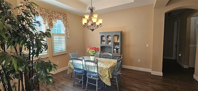 dining space featuring baseboards, a tray ceiling, arched walkways, dark wood-type flooring, and a notable chandelier