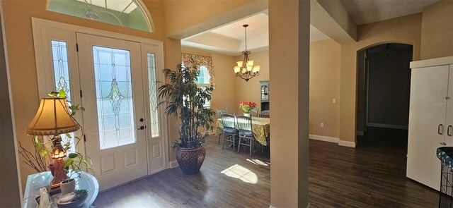 foyer entrance featuring baseboards, dark wood finished floors, arched walkways, a notable chandelier, and a raised ceiling