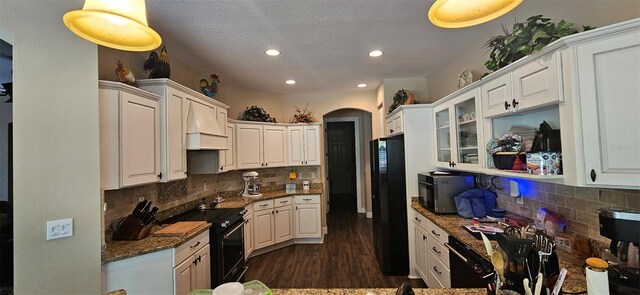 kitchen with recessed lighting, dark stone countertops, arched walkways, white cabinets, and black appliances