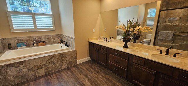 bathroom with toilet, a sink, wood finished floors, double vanity, and a bath