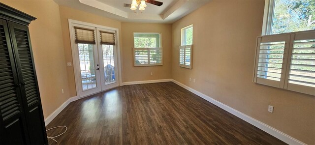 empty room featuring baseboards, ceiling fan, a tray ceiling, french doors, and dark wood-style floors