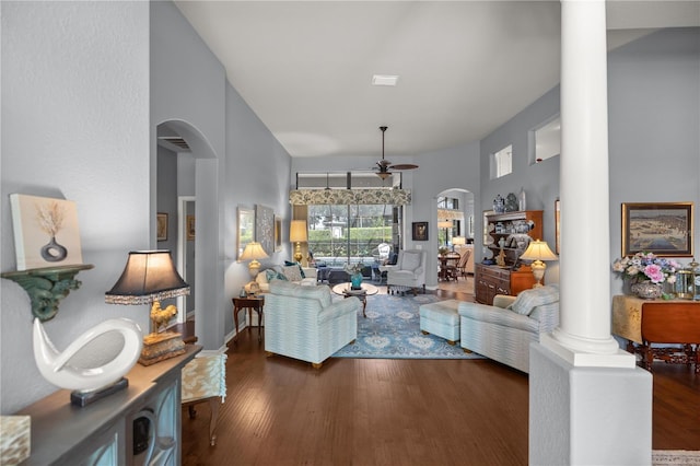 living room featuring dark hardwood / wood-style flooring, a towering ceiling, ornate columns, and ceiling fan