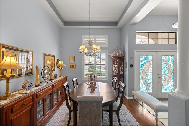 dining space featuring french doors, decorative columns, a raised ceiling, wood-type flooring, and a chandelier