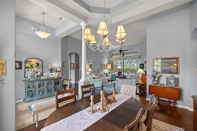 dining area featuring decorative columns, a towering ceiling, ceiling fan with notable chandelier, and hardwood / wood-style flooring