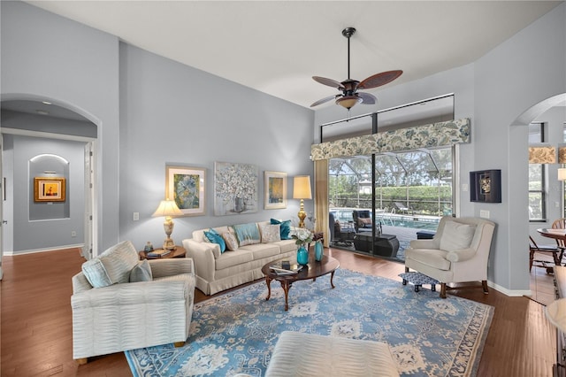 living room with ceiling fan, dark hardwood / wood-style flooring, and a towering ceiling