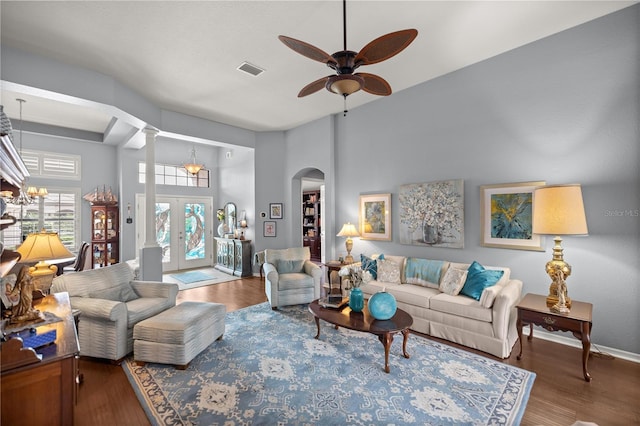 living room with french doors, decorative columns, hardwood / wood-style floors, a towering ceiling, and ceiling fan with notable chandelier