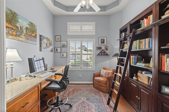 home office with a tray ceiling, ceiling fan, and hardwood / wood-style floors