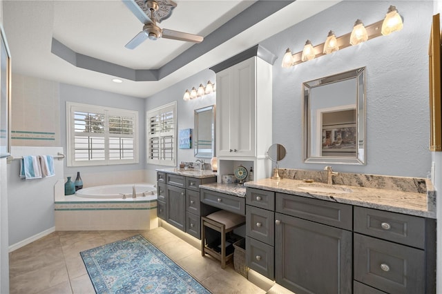 bathroom featuring vanity, a raised ceiling, tile patterned flooring, a relaxing tiled tub, and ceiling fan