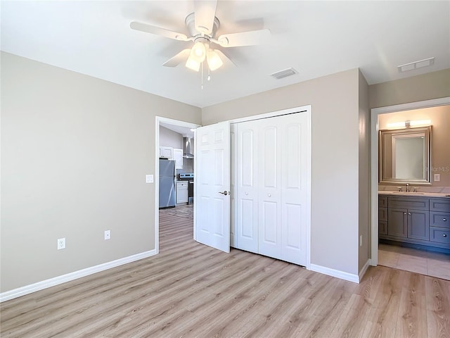 unfurnished bedroom with stainless steel fridge, a closet, light wood-type flooring, ceiling fan, and sink