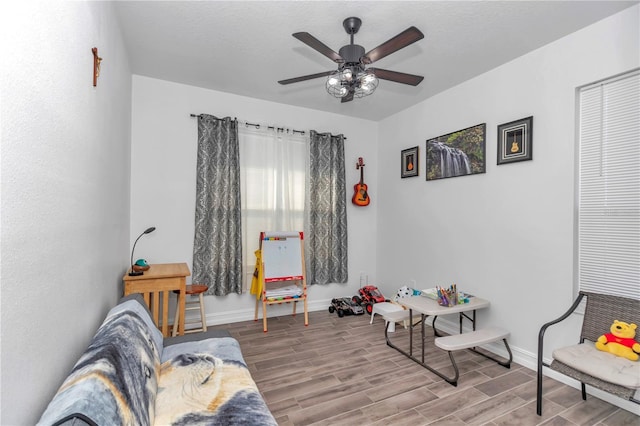 living area with ceiling fan, wood finish floors, a textured ceiling, and baseboards