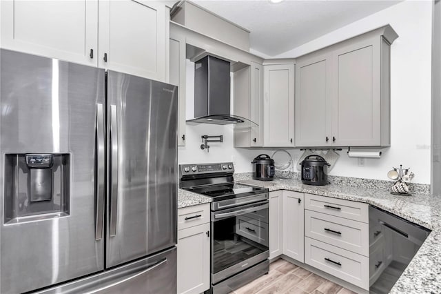 kitchen with light wood finished floors, gray cabinetry, appliances with stainless steel finishes, light stone countertops, and wall chimney exhaust hood