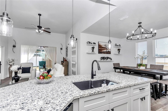 kitchen featuring light stone counters, hanging light fixtures, open floor plan, white cabinetry, and a sink