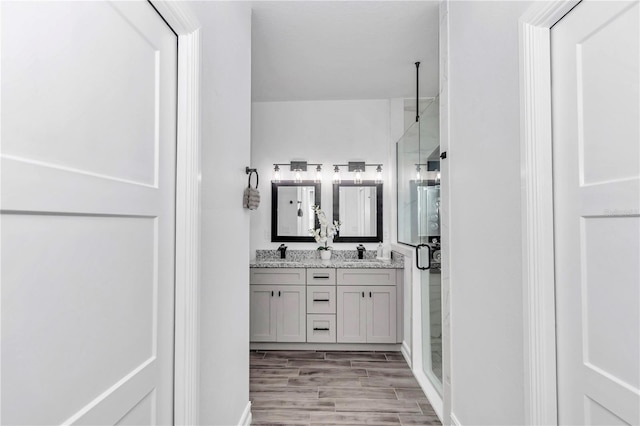 bathroom with a stall shower, double vanity, a sink, and wood finished floors