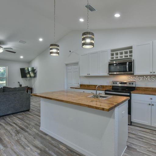 kitchen with wood counters, a center island with sink, appliances with stainless steel finishes, decorative light fixtures, and white cabinets