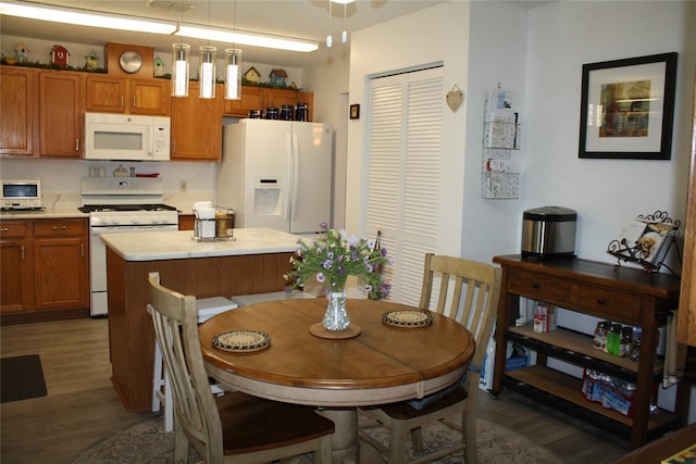 kitchen featuring white appliances, hanging light fixtures, and dark wood-type flooring