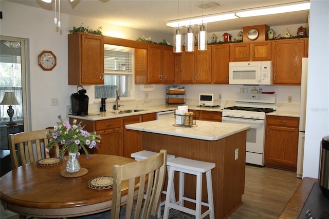 kitchen with white appliances, dark hardwood / wood-style floors, hanging light fixtures, a kitchen island, and sink