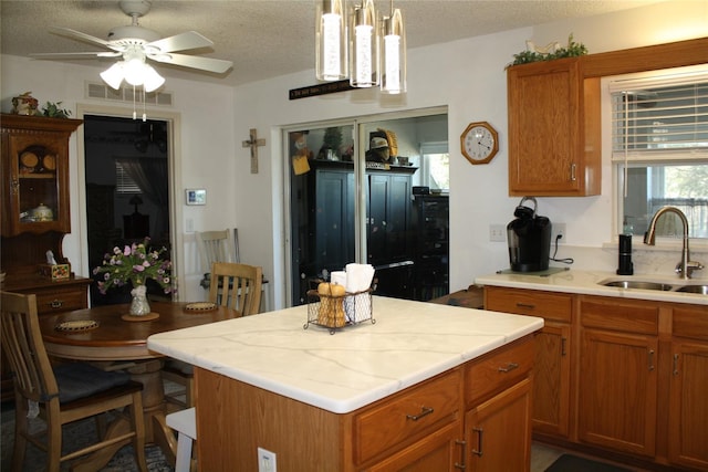 kitchen with sink, ceiling fan with notable chandelier, decorative light fixtures, and a textured ceiling