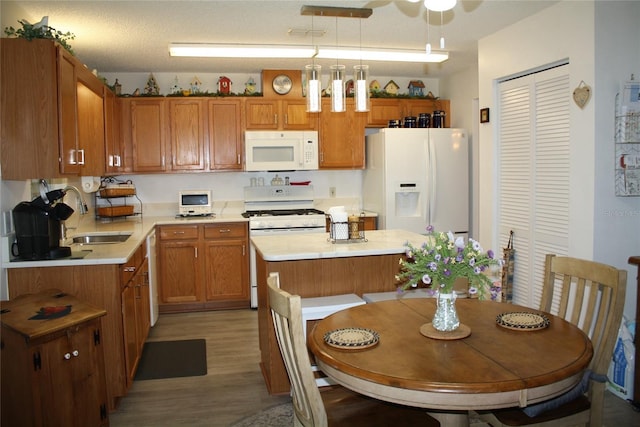 kitchen with white appliances, light hardwood / wood-style floors, a center island, sink, and decorative light fixtures