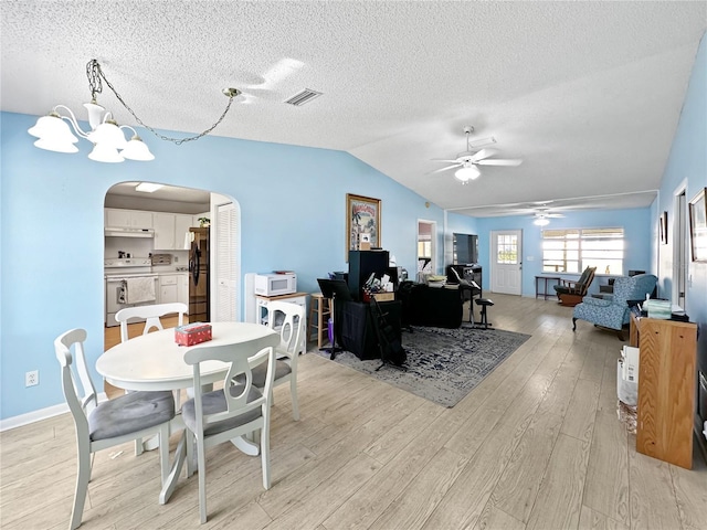 dining space featuring ceiling fan with notable chandelier, a textured ceiling, light hardwood / wood-style flooring, and vaulted ceiling