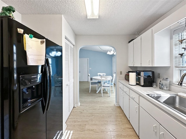 kitchen with white cabinetry, light hardwood / wood-style floors, black fridge with ice dispenser, a textured ceiling, and sink