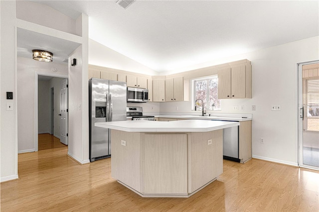 kitchen with sink, appliances with stainless steel finishes, vaulted ceiling, a kitchen island, and light wood-type flooring