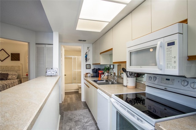 kitchen with light wood-type flooring, a skylight, white appliances, sink, and white cabinetry