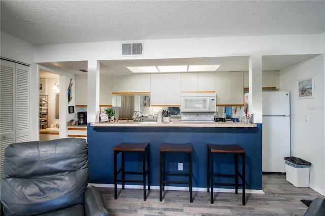 kitchen with a textured ceiling, white appliances, dark wood-type flooring, white cabinetry, and a breakfast bar area