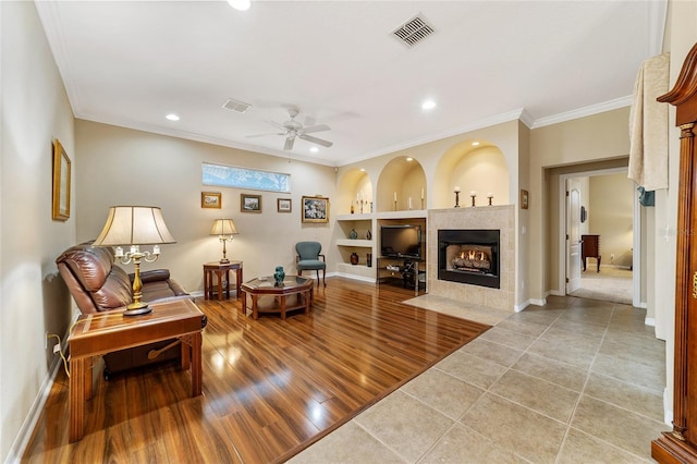 living room featuring a fireplace, ceiling fan, light hardwood / wood-style flooring, built in shelves, and crown molding