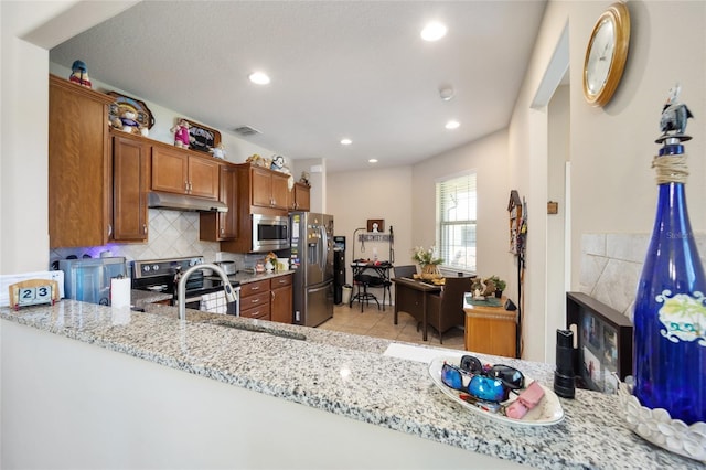 kitchen featuring backsplash, sink, light stone countertops, kitchen peninsula, and stainless steel appliances