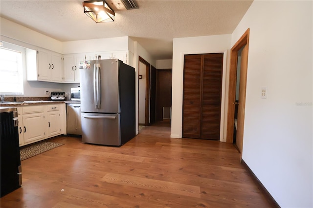 kitchen with a textured ceiling, white cabinetry, light wood finished floors, and appliances with stainless steel finishes