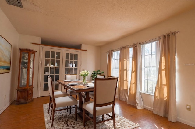 dining area with baseboards, visible vents, a textured ceiling, and light wood-style flooring